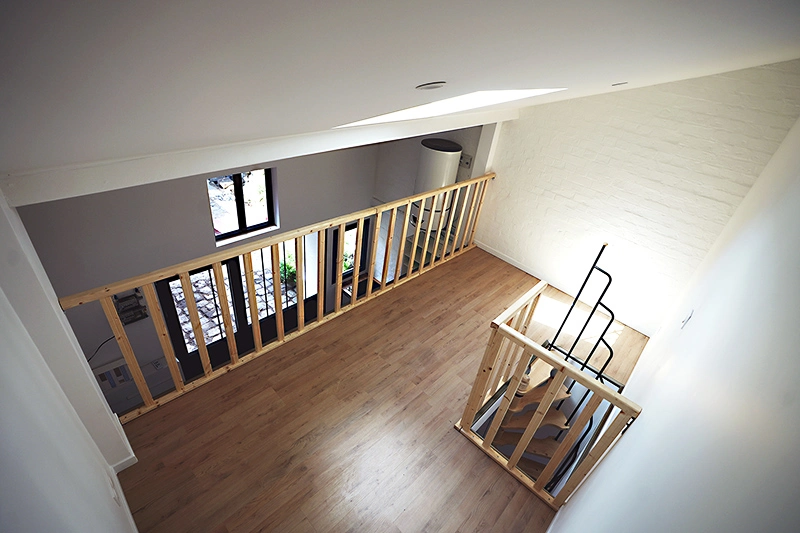 Vue de la mezzanine en bois servant d’espace nuit, avec parquet, garde-corps sécurisé et aménagement chaleureux sous toit isolé.