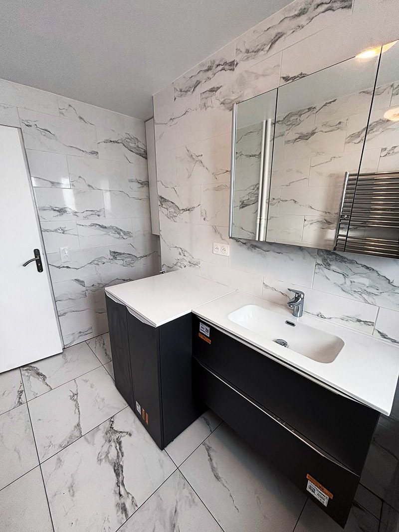 Vue latérale de la salle de bain rénovée avec meuble et carrelage blanc