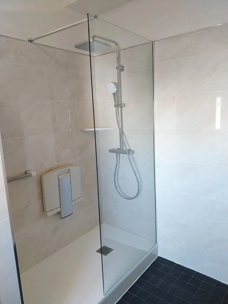 Douche à l’italienne avec siège mural, barre d’appui et paroi vitrée