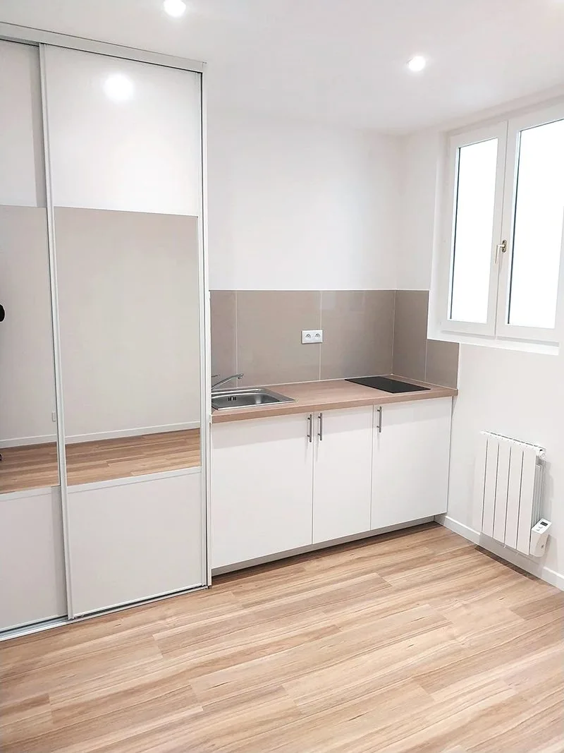 Vue de la pièce principale rénovée avec cuisine équipée, sol en carrelage imitation parquet et peinture neuve.