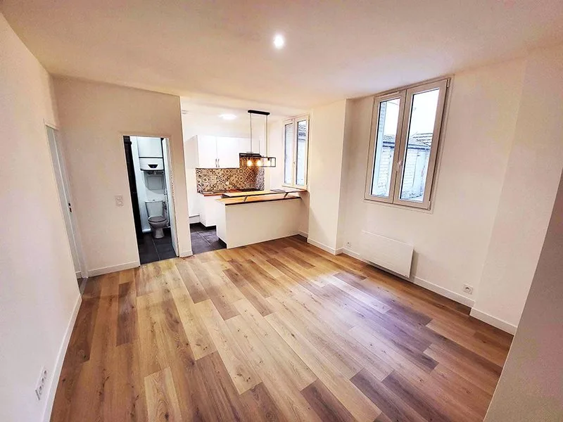 Salon d’un appartement rénové, avec vue dégagée sur la cuisine ouverte, créant un espace de vie fluide et lumineux.