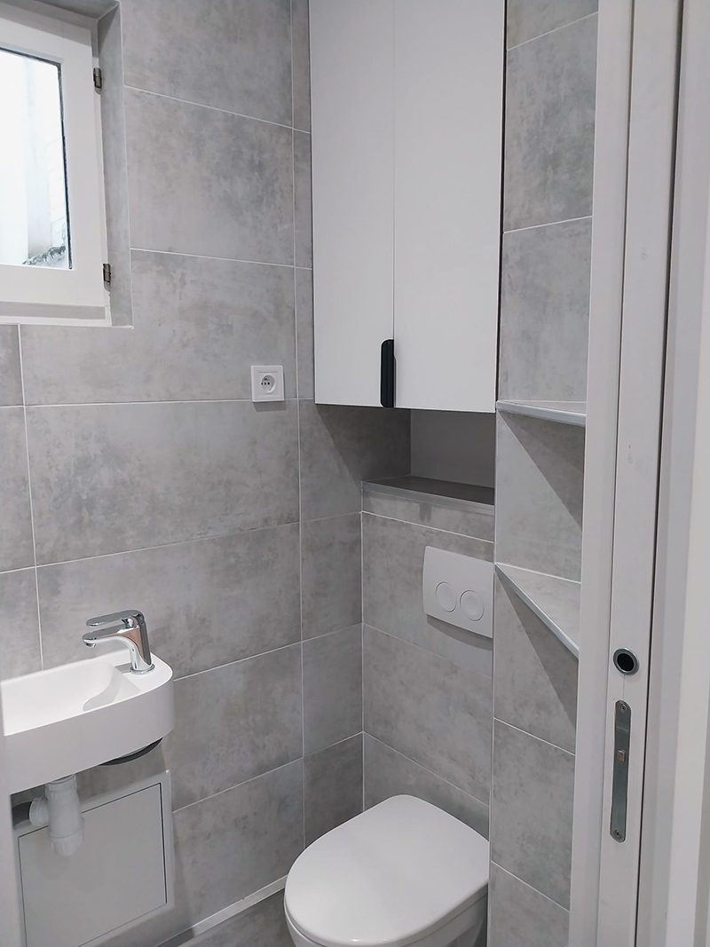 Salle de bain fonctionnelle avec toilettes suspendus, lavabo moderne et rangements intégrés.