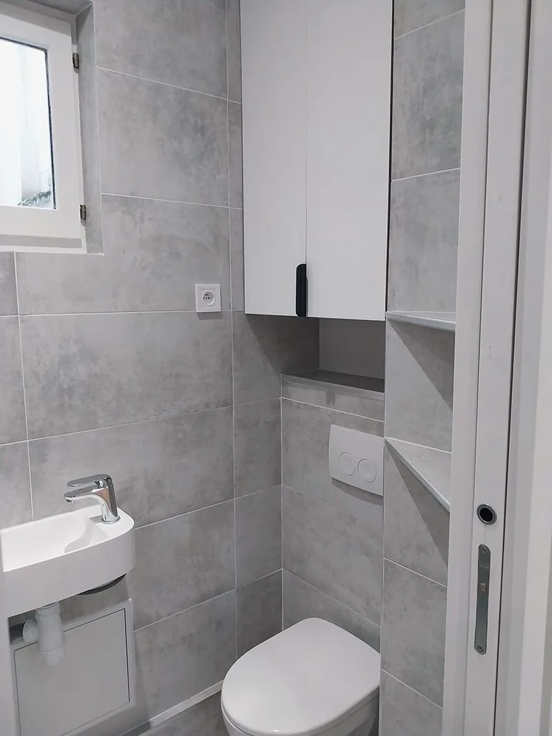 Salle de bain fonctionnelle avec toilettes suspendus, lavabo moderne et rangements intégrés.