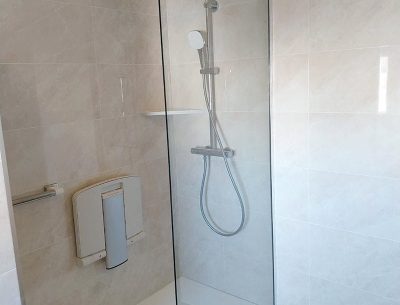 Douche à l’italienne avec siège mural, barre d’appui et paroi vitrée