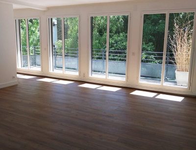 Salon lumineux après rénovation, sol PVC imitation parquet et murs repeints.