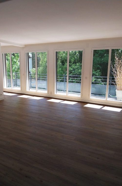 Salon lumineux après rénovation, sol PVC imitation parquet et murs repeints.